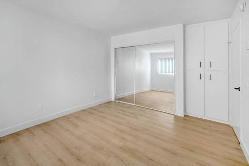 a bedroom with white walls and wood floors and a closet