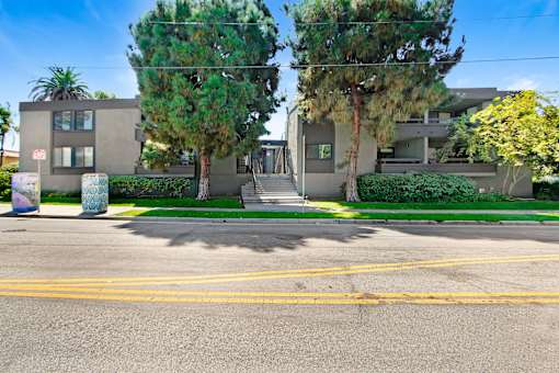 A street view of a residential area with two houses, trees, and a clear sky.
