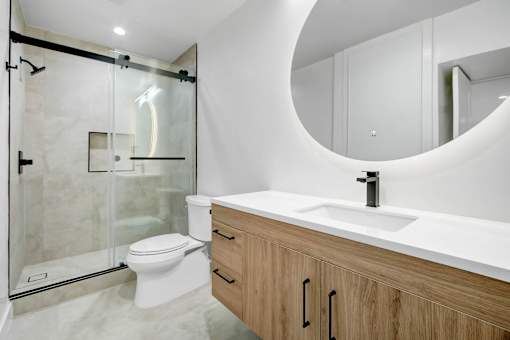 A modern bathroom with a walk-in shower, toilet, and a round mirror.