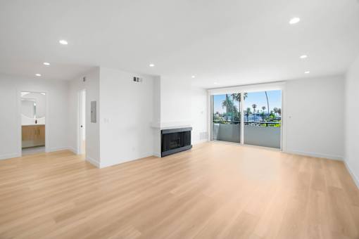 A spacious room with wooden flooring and a large window overlooking a beach.
