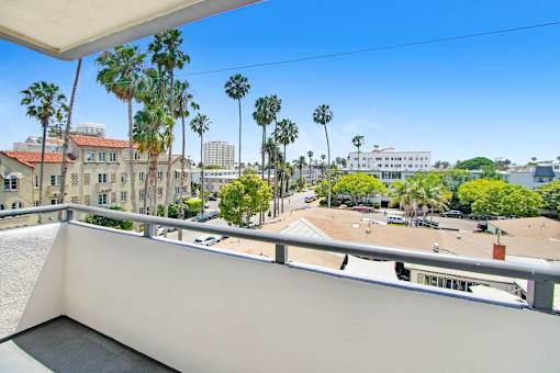 A balcony overlooks a parking lot and palm trees.