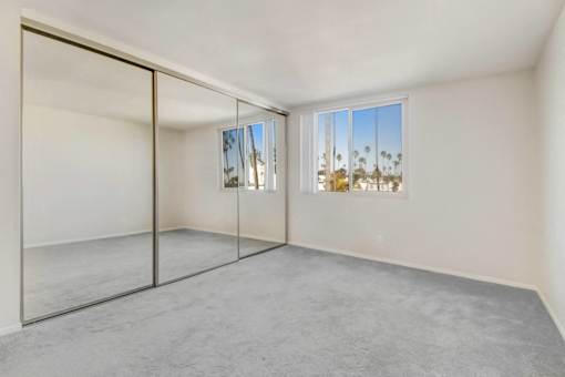 A room with a sliding glass door leading to a balcony with a view of palm trees.