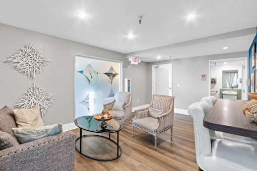A living room with a grey couch, a glass table, and a white chair.