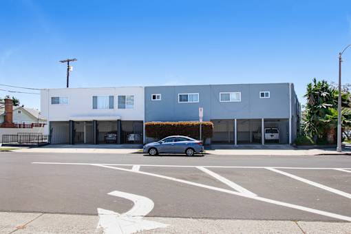 A silver car is parked in front of a grey building.