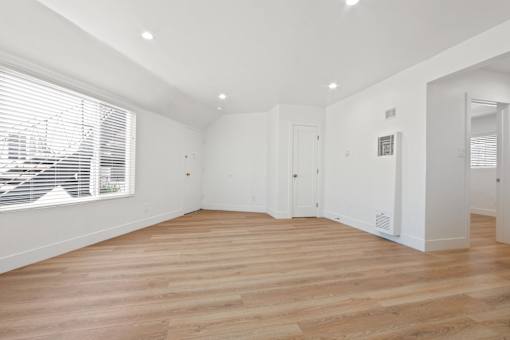 A spacious room with wooden flooring and white walls.