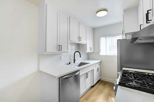 A kitchen with white cabinets and a stainless steel sink and stove.