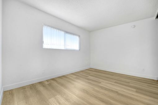 A room with wooden flooring and a window with blinds.