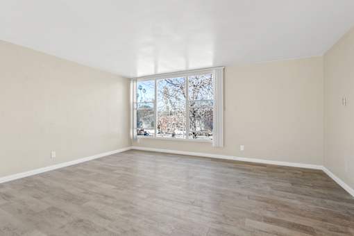 Empty room with a large window and wooden flooring.
