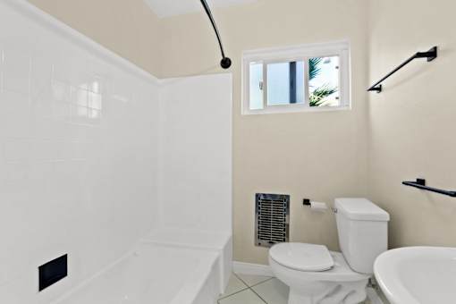 A white bathroom with a toilet, tub, and window.