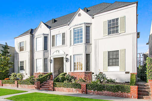 A white two-story house with a red brick wall in front.