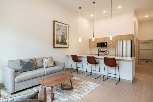 A living room with a grey couch, a coffee table, and a bar area with stools.