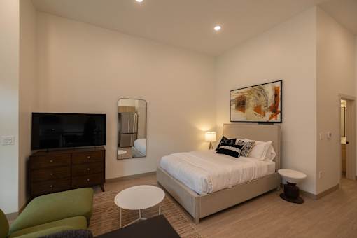 A bedroom with a bed, a green chair, and a television.