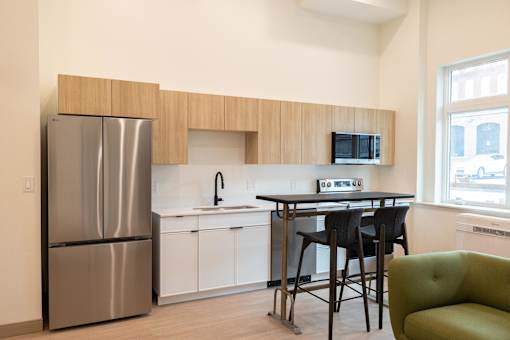 A kitchen with a stainless steel refrigerator, a white dishwasher, a black chair, and a green armchair.
