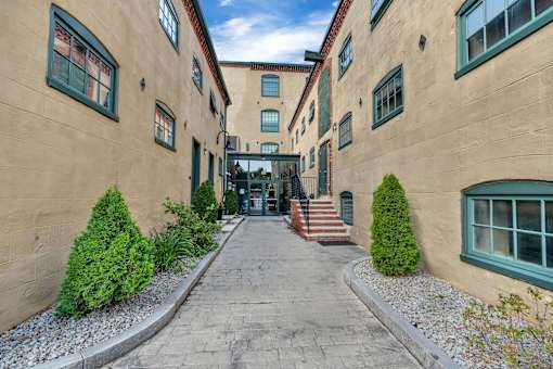 A long, narrow alleyway between two tan buildings with green trim and steps leading to the entrance.