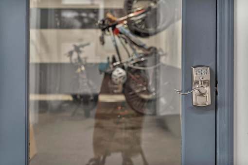 A person is standing in front of a glass door with a bicycle reflected in it.