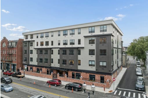 A street view of a multi-story building with cars parked in front.