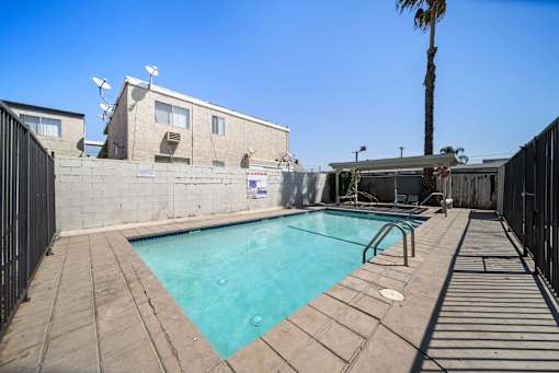 A pool surrounded by a black fence and concrete walkway.