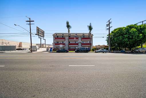 A street view with a building in the background and cars parked on the side of the road.