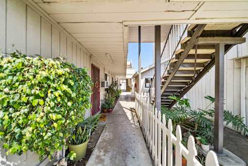 A long, narrow hallway with a white picket fence and a staircase on the right.