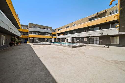 A courtyard surrounded by buildings with a fence and a bird on the ground.