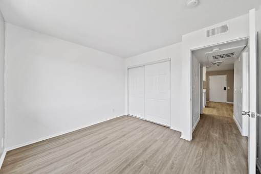 A room with white walls and wooden flooring with a door on the left and another door on the right.