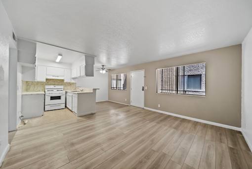 A large empty room with wooden flooring and a kitchen area in the background.