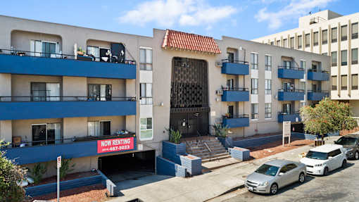 A building with a sign that says "Now Renting" is in front of a car.