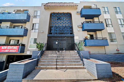 A building with a black gate and a sign that says "Now Renting" in front of it.