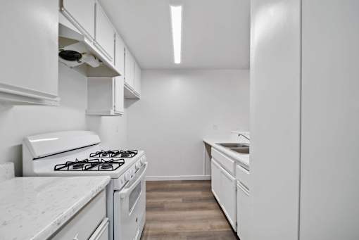 A white kitchen with a stove, sink, and cabinets.