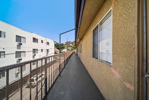 A long balcony with a black railing and a tan wall.