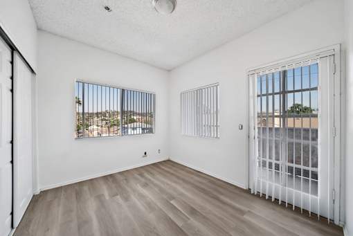 A room with white walls and wooden flooring, featuring two windows with metal bars.