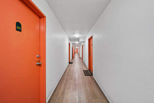 A long hallway with orange doors and a white wall.