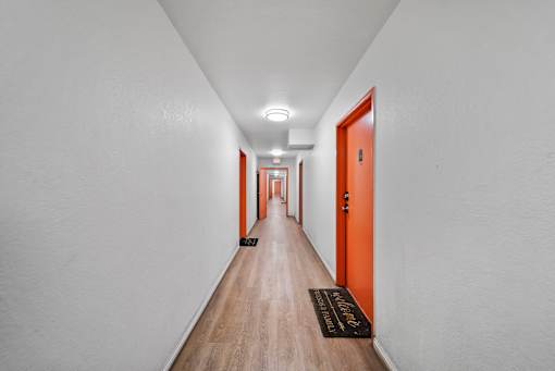 A long hallway with orange doors and a black doormat.