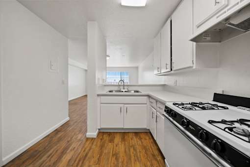 A kitchen with a stove, sink, and cabinets.