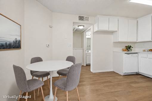 A white dining table with grey chairs in a white kitchen.