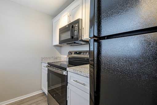 A black refrigerator stands next to a white oven and microwave in a kitchen at Imperial Gardens Apartments, Florida