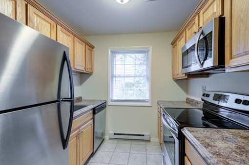 A kitchen with a stainless steel refrigerator and wooden cabinets at Rivercrest Apartments, New Jersey