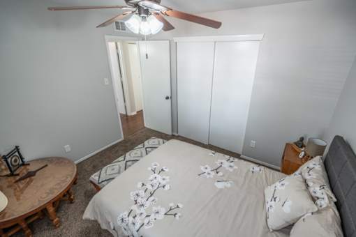 A bedroom with a bed, a ceiling fan, and a small table.