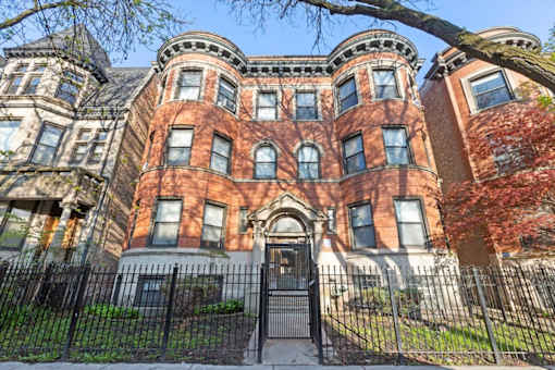 A large, red brick Victorian style house with a black iron fence.
