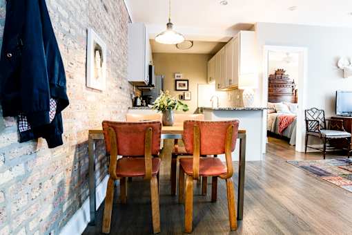 A kitchen with a table and chairs in the foreground and a brick wall on the left.