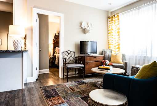 A living room with a blue couch, a wooden dresser, a television, and a rug.