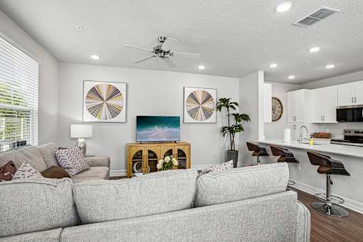 A living room with a grey couch, a fan, and a painting on the wall.
