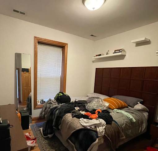 A bedroom with a messy bed and a window with blinds.