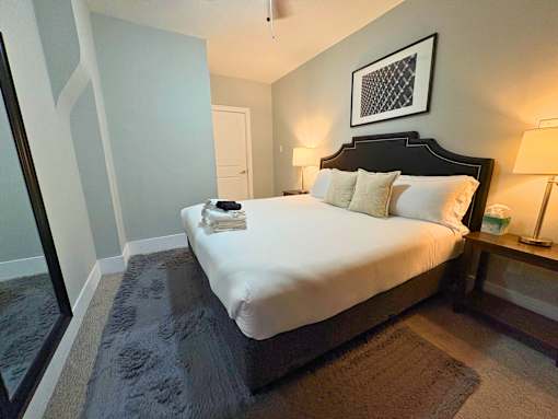 A bed with white sheets and a black headboard with a picture above it.