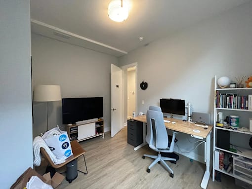 A room with a desk, chair, and a television.
