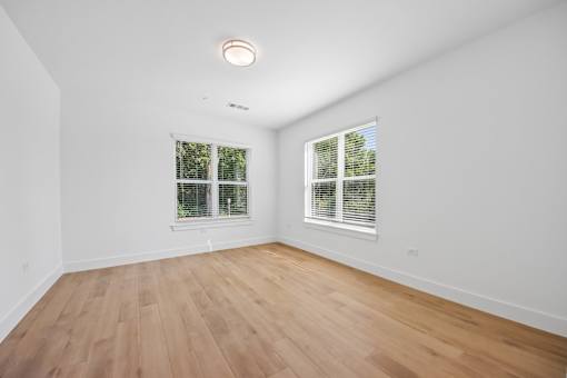 A room with wooden flooring and two windows.