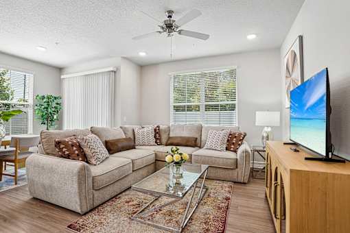 A living room with a beige couch, a glass coffee table, and a flat-screen TV on a wooden stand.
