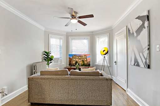 A living room with a couch, a fan, and a painting on the wall.