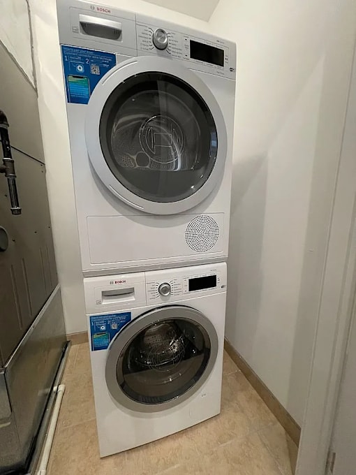 A white front loading washing machine with a black door is stacked on top of another white front loading washing machine with a black door.