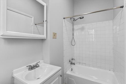 A white bathroom with a sink, mirror, and bathtub.